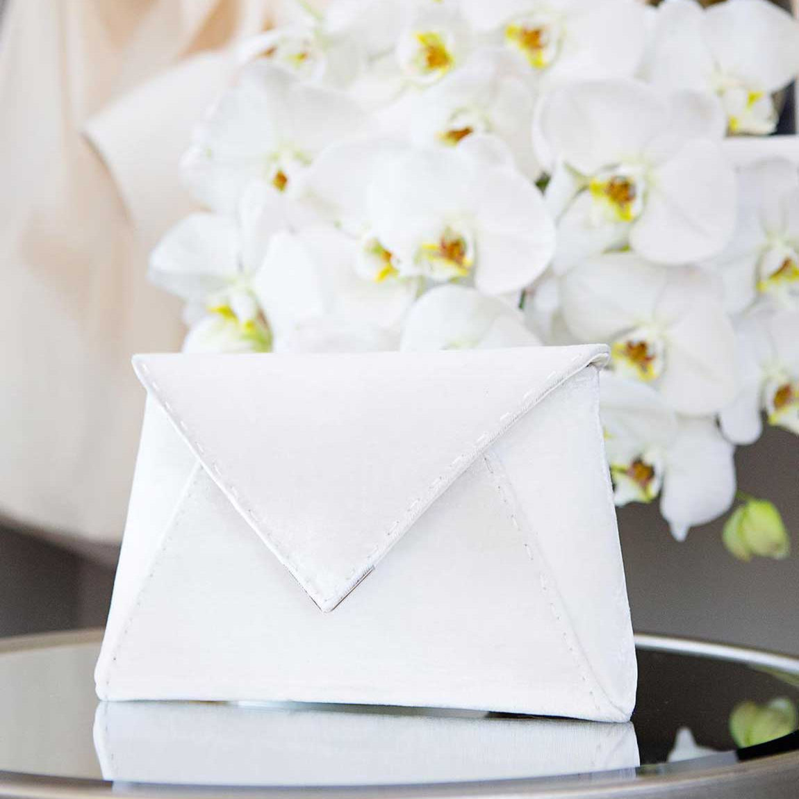 White orchids in a decorative container on a reflective surface with a blurred background