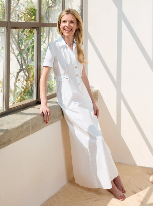 Tyler Ellis in a white outfit standing in a bright room with large windows.